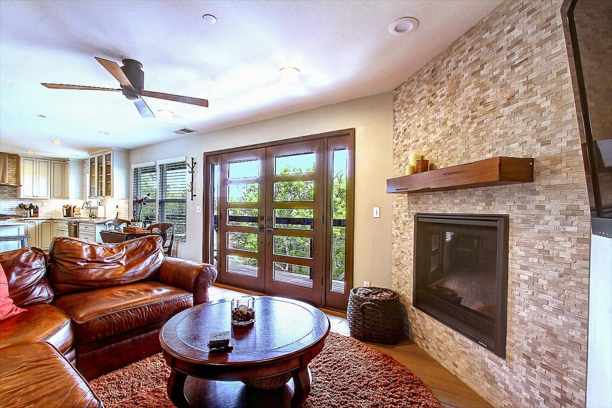 Family room with leather sectional, stacked-stone fireplace, and glass double doors to a deck