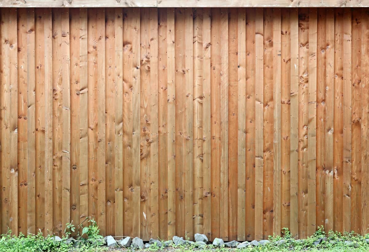 Vertical wood plank fence with greenery and small stones along its base
