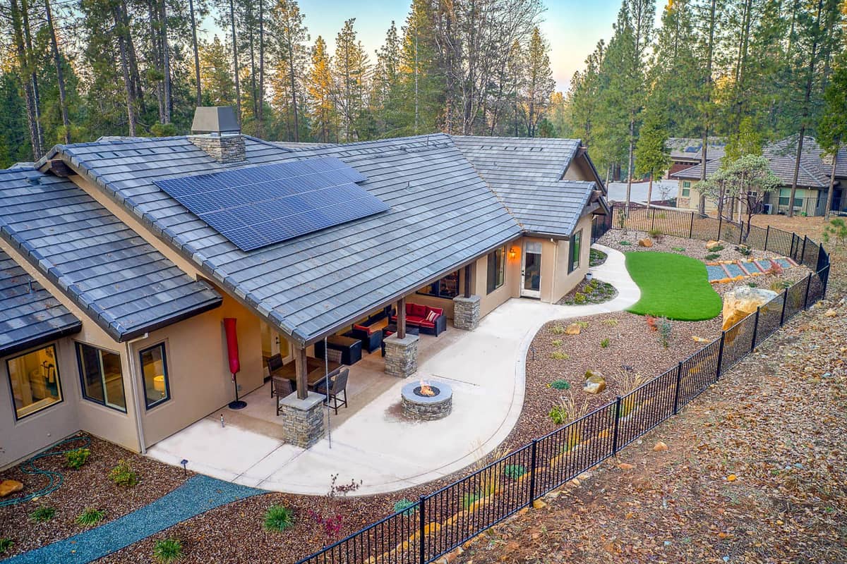 Aerial view of a home with rooftop solar panels, covered patio, fire pit, and fenced yard