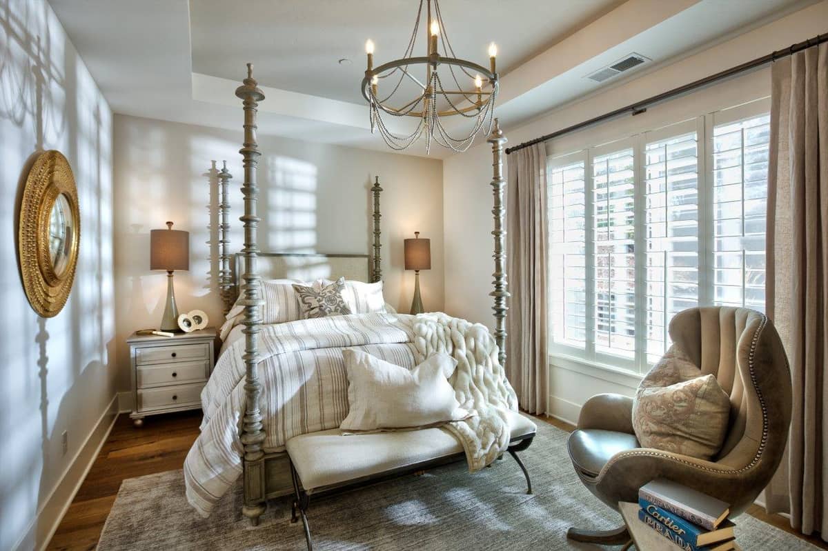 Elegant bedroom with four-poster bed, chandelier, plantation shutters, and cozy reading chair