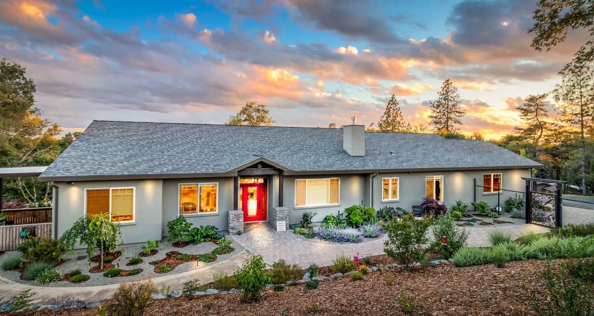 Single-story home with red front door and drought-tolerant landscaping under a sunset sky