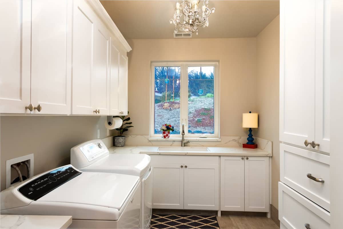 White laundry room with washer and dryer, sink under a window, and abundant cabinet storage