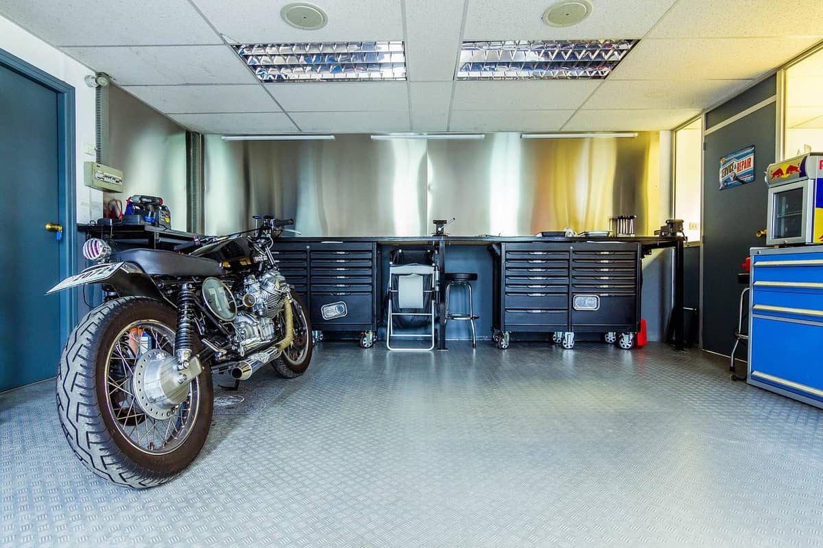 Organized garage workshop with motorcycle, rolling tool chests, and stainless workbench wall