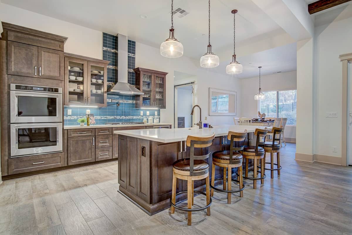 Kitchen island with bar-stool seating, pendant lights, blue tile backsplash, and double wall ovens