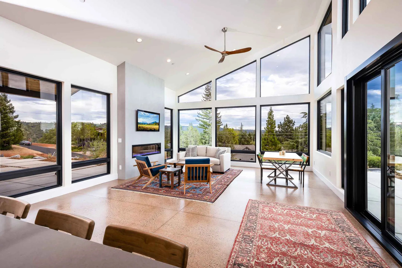 Vaulted great room with a wall of black-framed windows looking out to pines and foothills, polished concrete floors and a linear fireplace