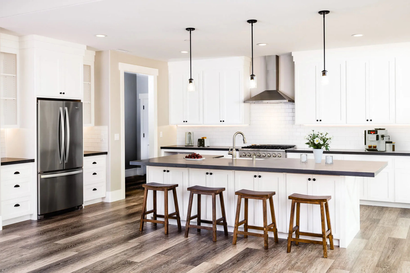Bright white kitchen with a long island, four wood stools, pendant lights and wide-plank floors in a Sherman custom home